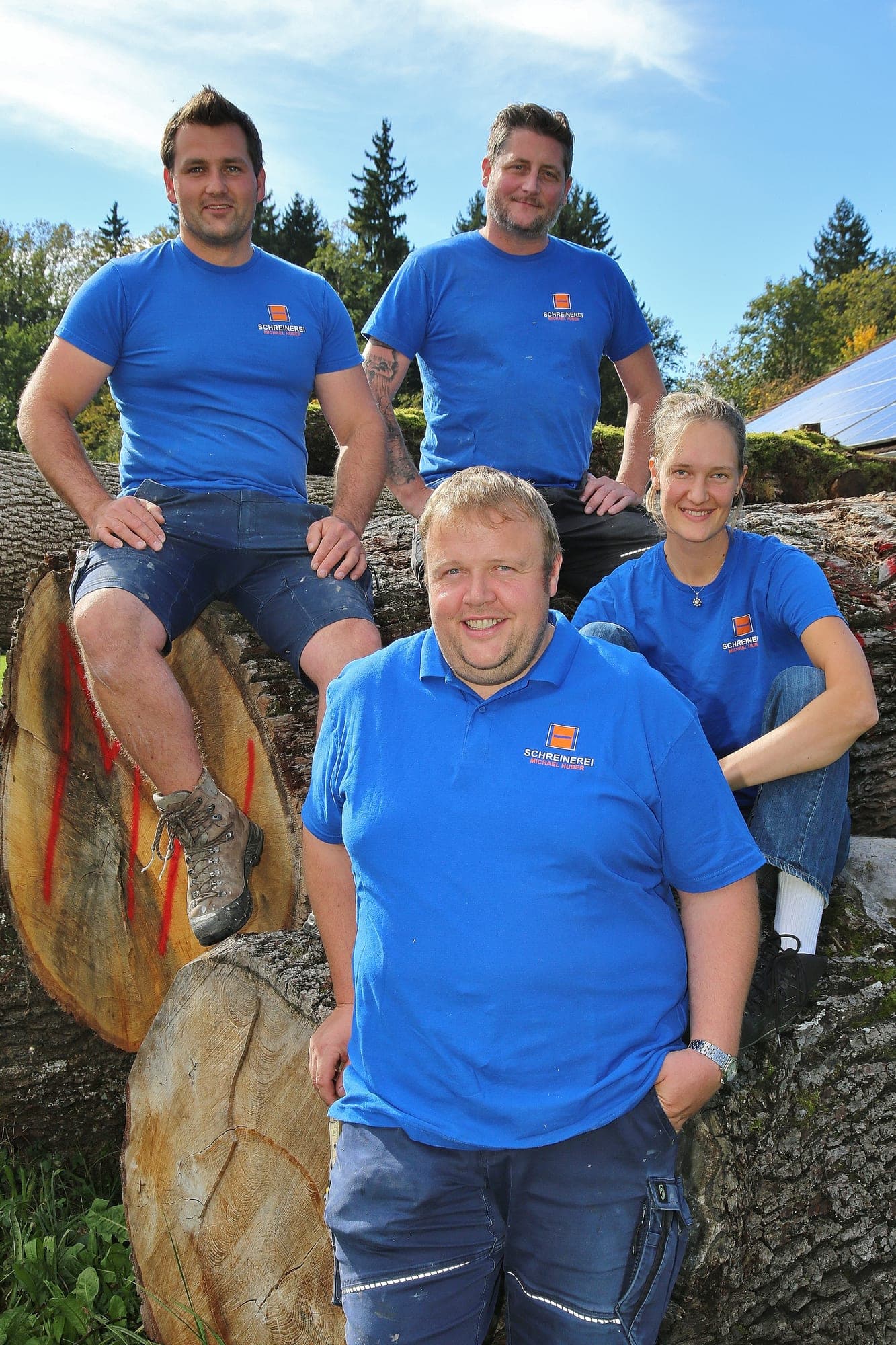 Das Team draußen auf einem Holzstamm vor Bäumen und blauem Himmel