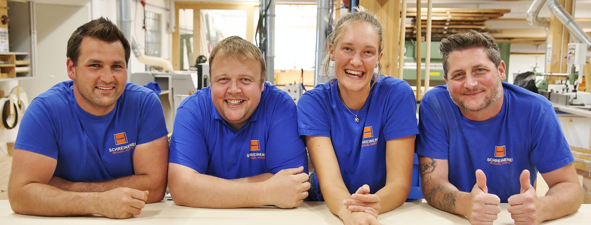 Vier aus dem Team lehnen lachend auf einer Werkbank